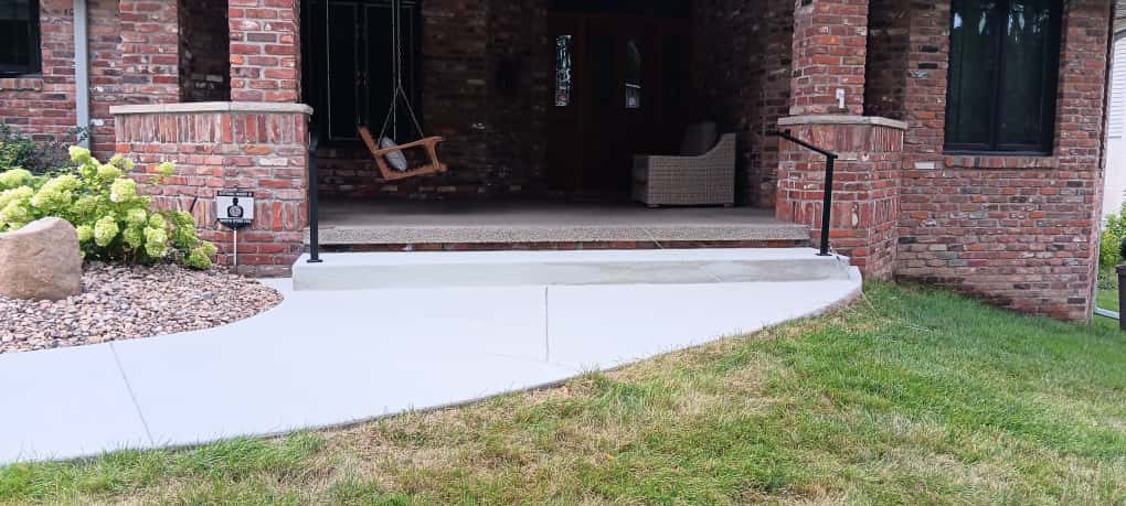 A poured concrete step and curved walkway at the front porch of a brick house.